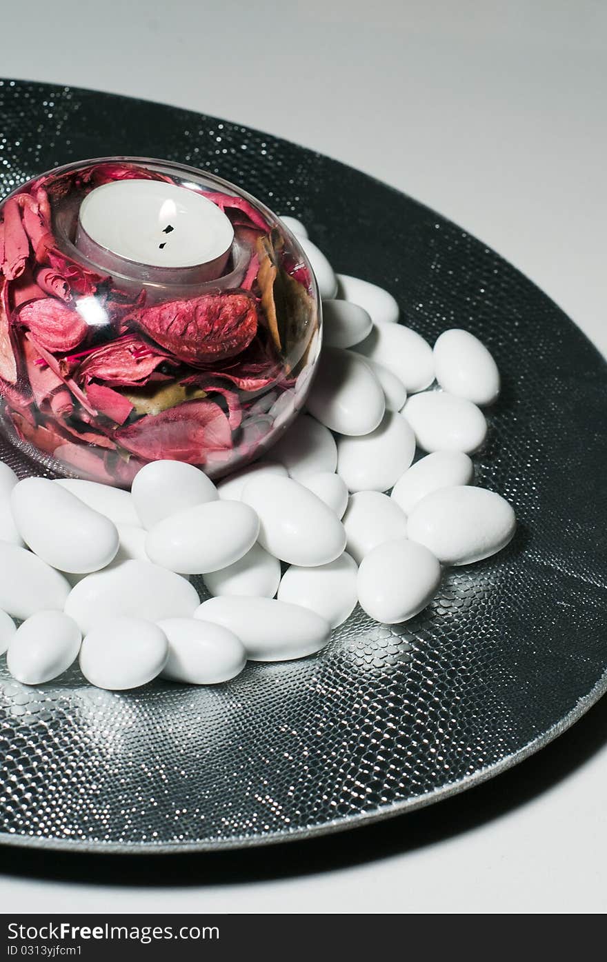 A round plate filled with sugared almonds and a lighted wax candle. A round plate filled with sugared almonds and a lighted wax candle