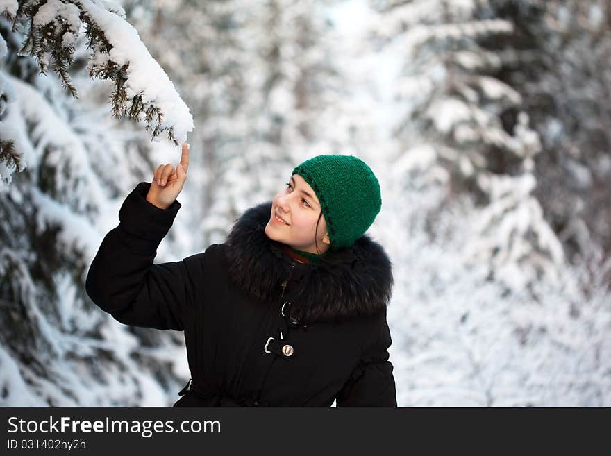 A girl in a warm fur coat walks in the winter forest