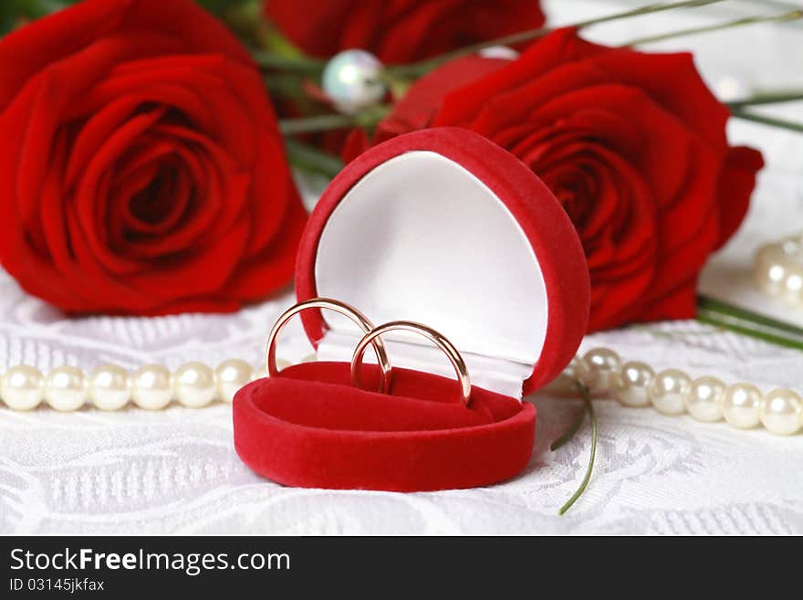 Wedding rings in red box against beautiful red roses on lace background