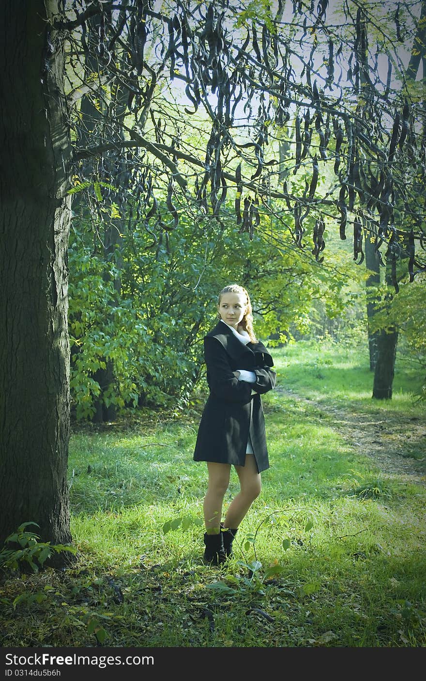 Girl stayning under the dark mysterious tree in the park