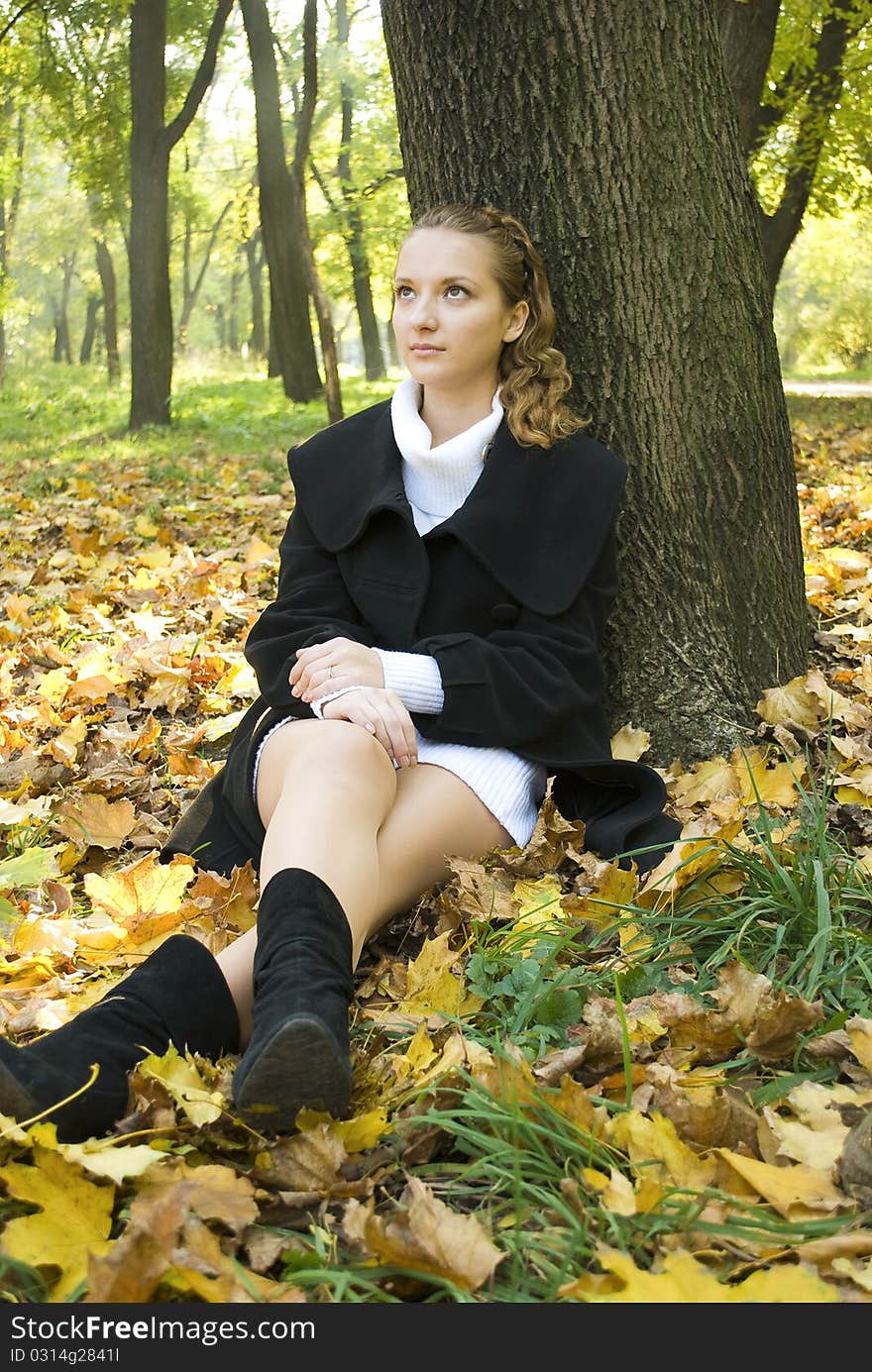 Pensive teen girl sits under the tree among gold leaves in autumn park. Pensive teen girl sits under the tree among gold leaves in autumn park