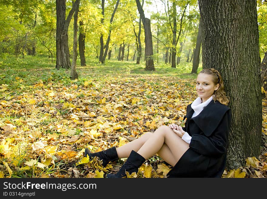 Teen girl sits under the tree among gold leaves in autumn park. Teen girl sits under the tree among gold leaves in autumn park