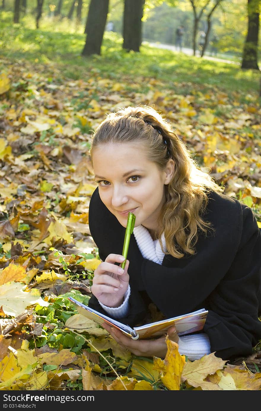 Teen girl lies in gold autumn park with her diary