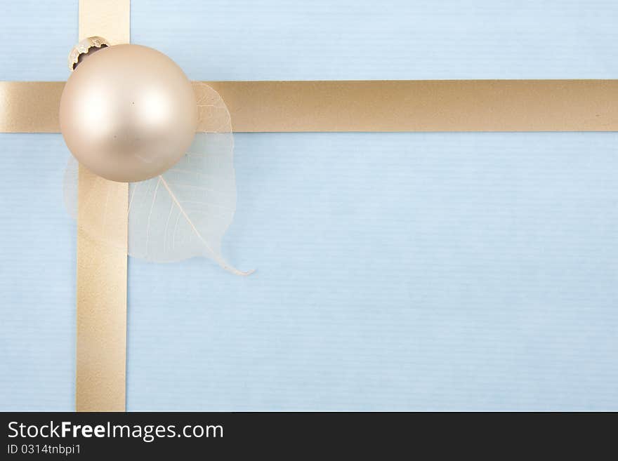 Christmas back ground with gold ribbon on light blue paper with a golden ball on a leaf at the left. Christmas back ground with gold ribbon on light blue paper with a golden ball on a leaf at the left