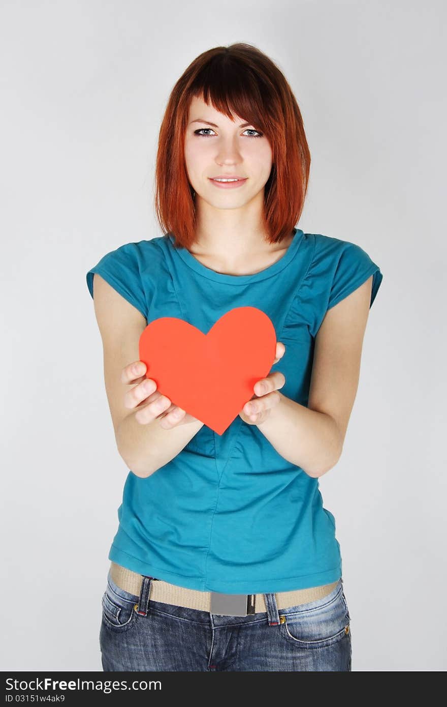 Young redhead girl holding red paper heart, looking at camera, half body