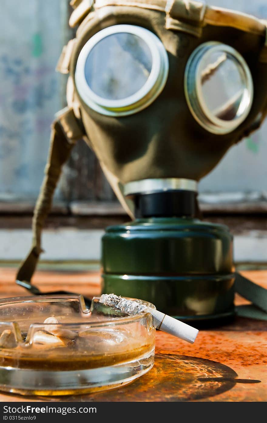 Cigarette with pot and gasmask in background on rusty table