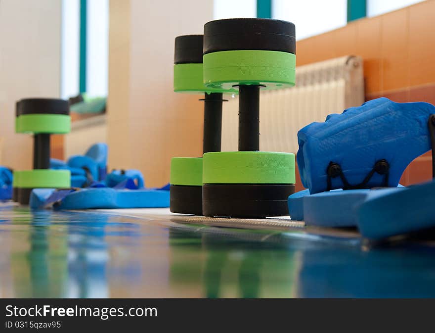 Equipment for aqua aerobics on pool side. woman stretching on background