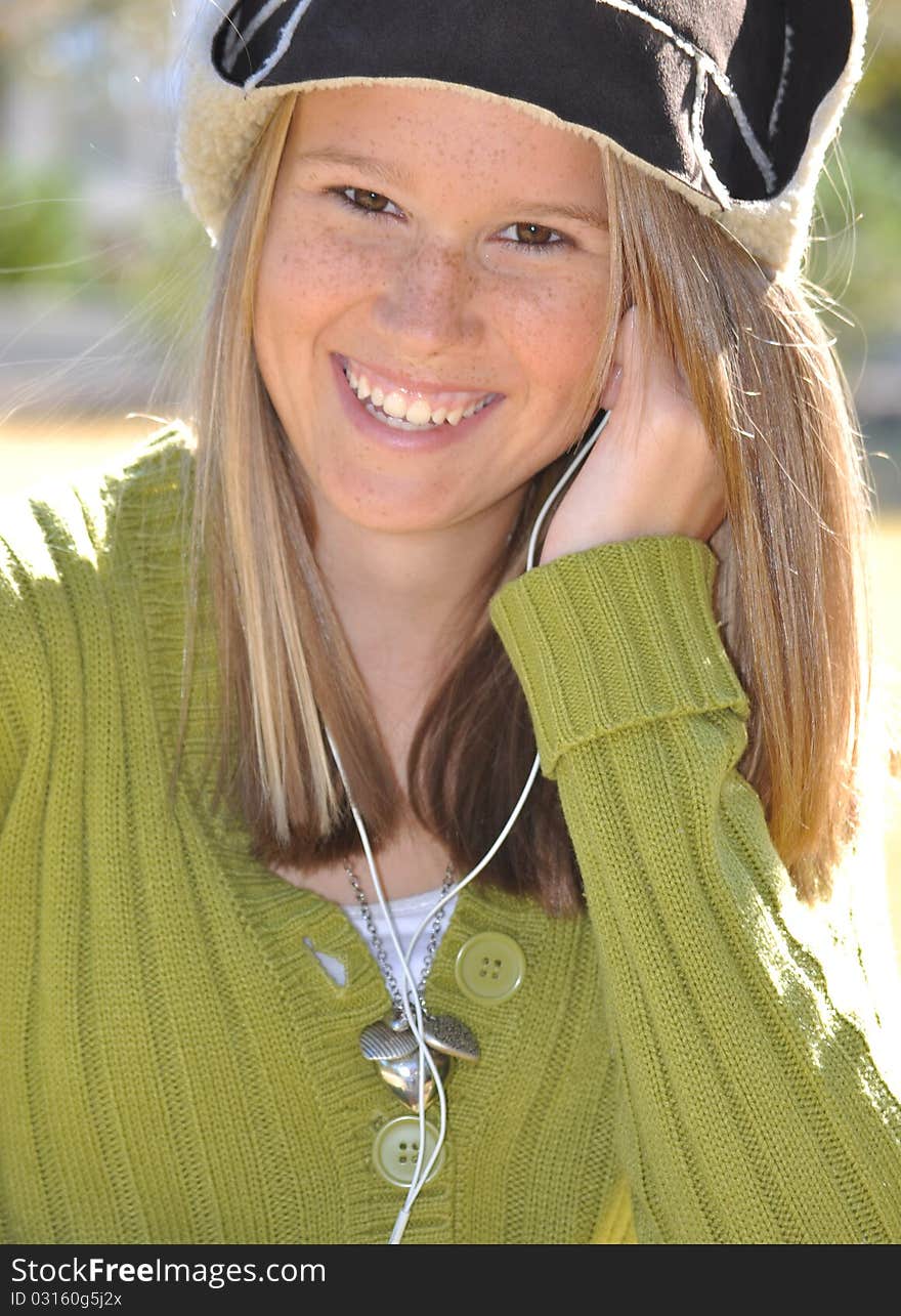 Pretty teen girl with long blonde hair wearing a wool hat and smiling as she listens to tunes on her ear buds. Pretty teen girl with long blonde hair wearing a wool hat and smiling as she listens to tunes on her ear buds.