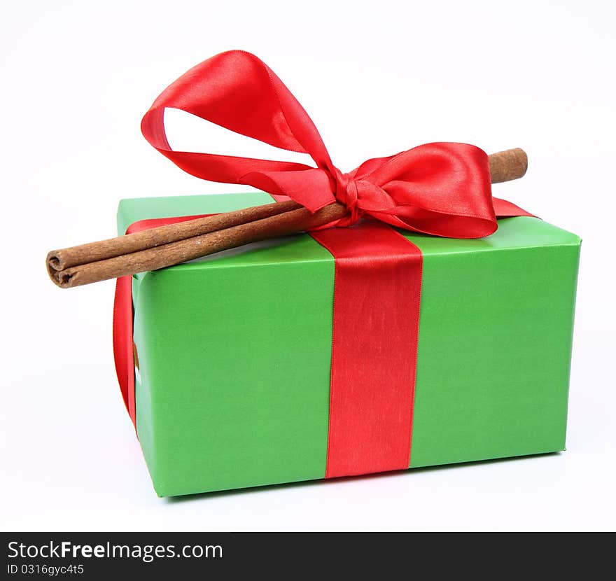 Gift in green wrapping with a red bow decorated with cinnamon stick on white background. Gift in green wrapping with a red bow decorated with cinnamon stick on white background