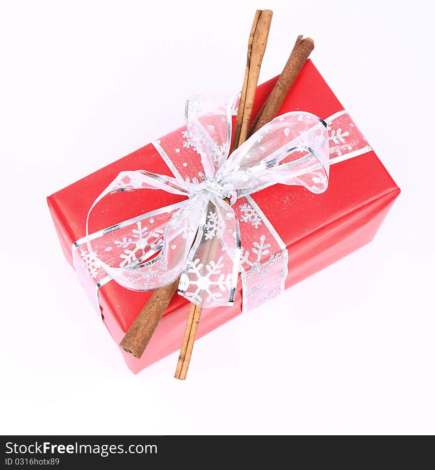 Gift in red wrapping with a silver bow decorated with cinnamon sticks on white background. Gift in red wrapping with a silver bow decorated with cinnamon sticks on white background