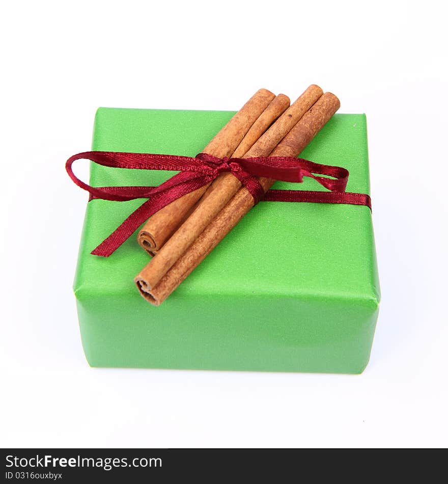 Gift in green wrapping with a red bow decorated with cinnamon sticks on white background. Gift in green wrapping with a red bow decorated with cinnamon sticks on white background