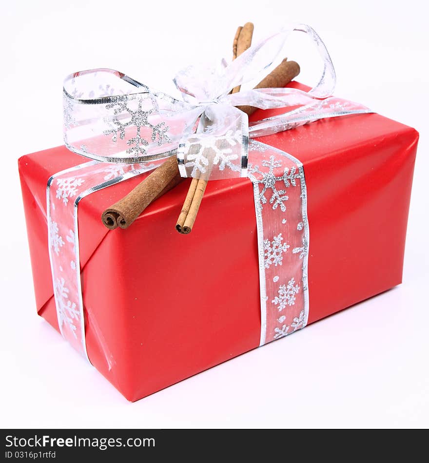 Gift in red wrapping with a silver bow decorated with cinnamon sticks on white background. Gift in red wrapping with a silver bow decorated with cinnamon sticks on white background