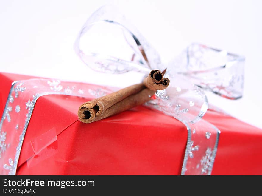 Gift in red wrapping with a silver bow decorated with cinnamon sticks in close up. Gift in red wrapping with a silver bow decorated with cinnamon sticks in close up