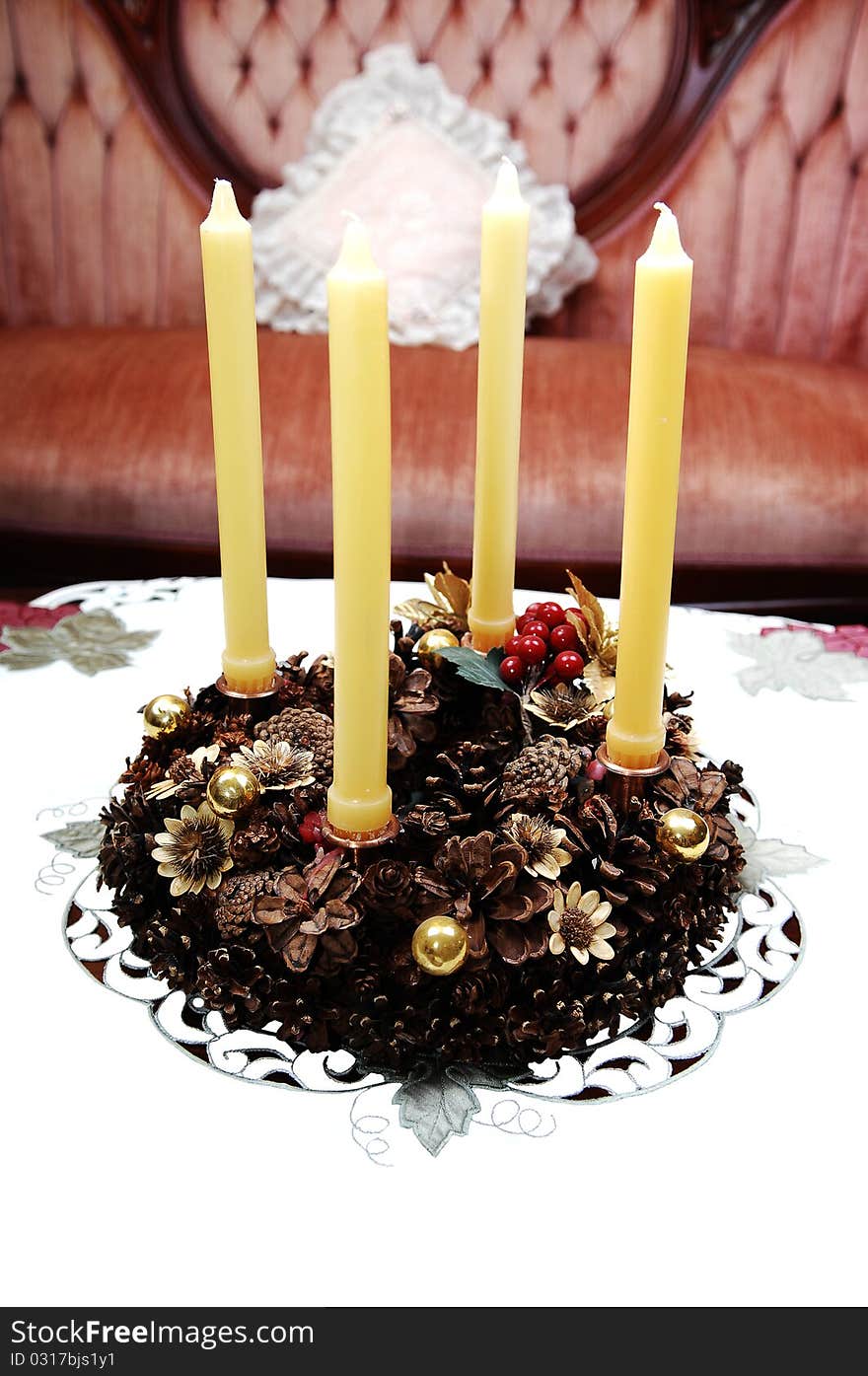 A old European adventskranz with four yellow candles, sitting on a table cloths and a pink sofa in background. A old European adventskranz with four yellow candles, sitting on a table cloths and a pink sofa in background..