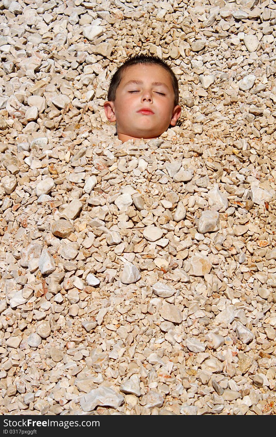 Boy buried in the pebbles on the beach