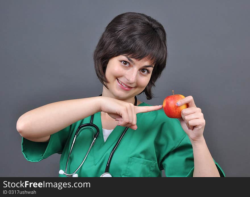 Attractive lady doctor pointing to a fresh apple on gray background