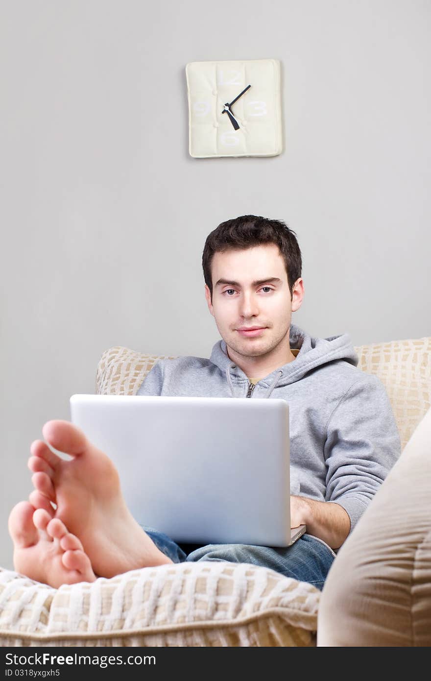 Smiling young man using laptop and lying on the sofa at home. Smiling young man using laptop and lying on the sofa at home