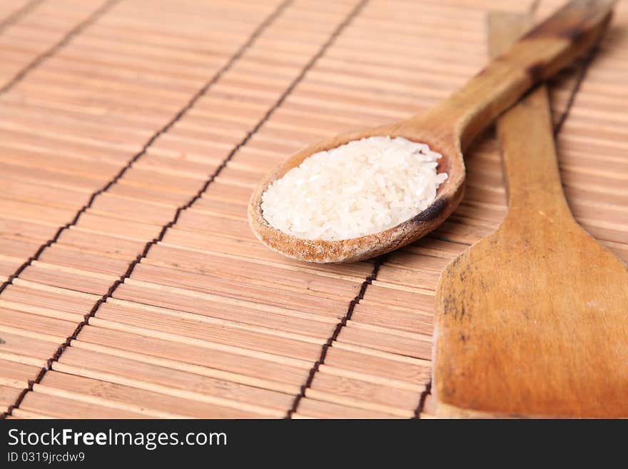 Spoon with rice and spoon empty over bamboo sticks background