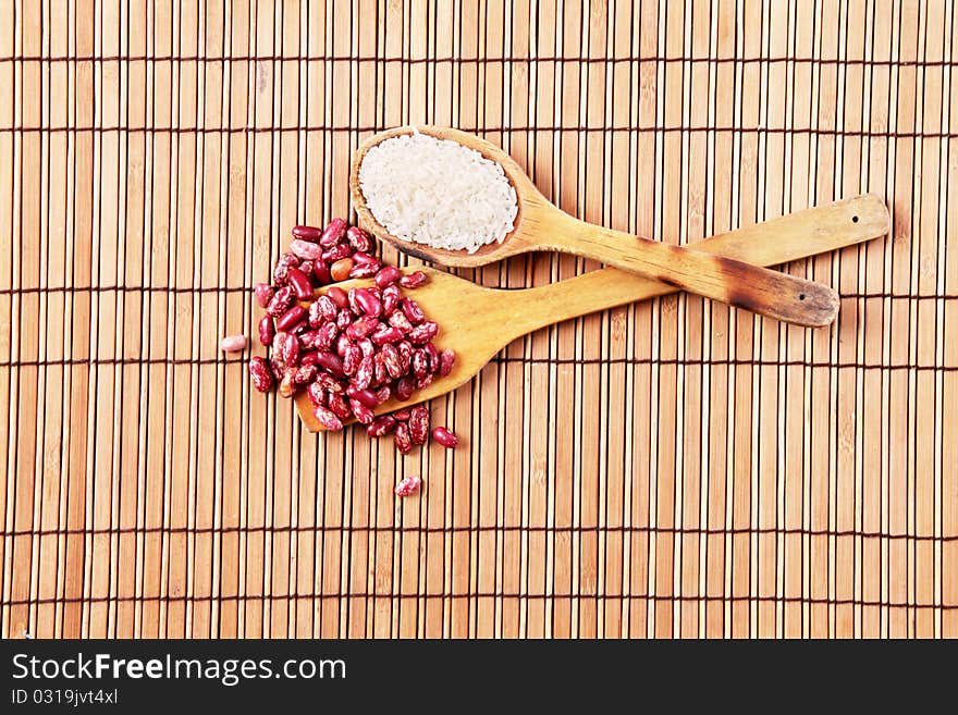 Wooden spoons with beans and rice over bamboo sticks background