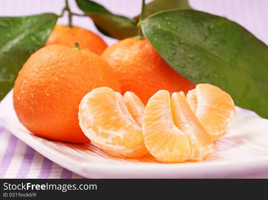 Whole and sectioned clementines over a white dish. Studio shot. Selective focus, extra-shallow DOF.