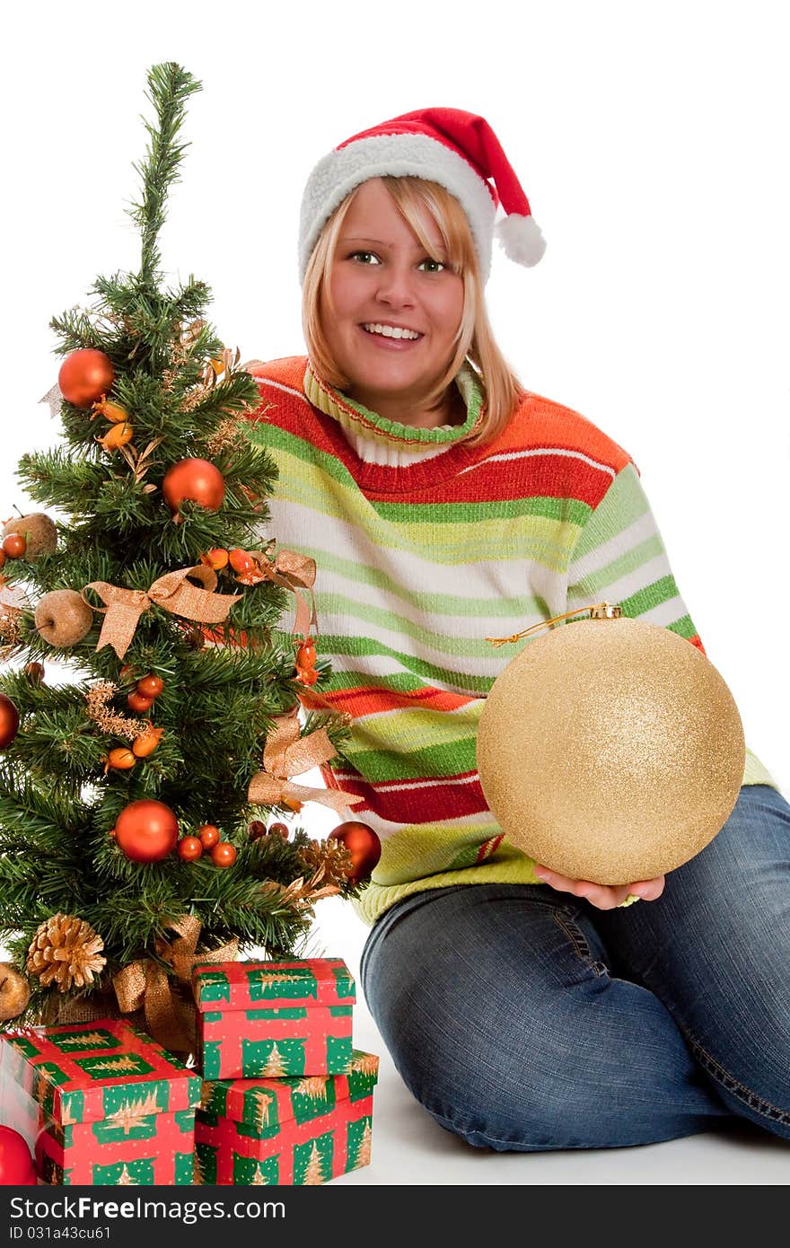 Young woman with santa hat sitting beside a christmas tree with christmas gifts - isolated. Young woman with santa hat sitting beside a christmas tree with christmas gifts - isolated