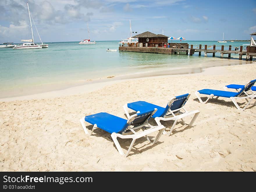 Empty blue beach chairs on a sandy beach overlooking the Caribbean Sea on a sunny day. Empty blue beach chairs on a sandy beach overlooking the Caribbean Sea on a sunny day.