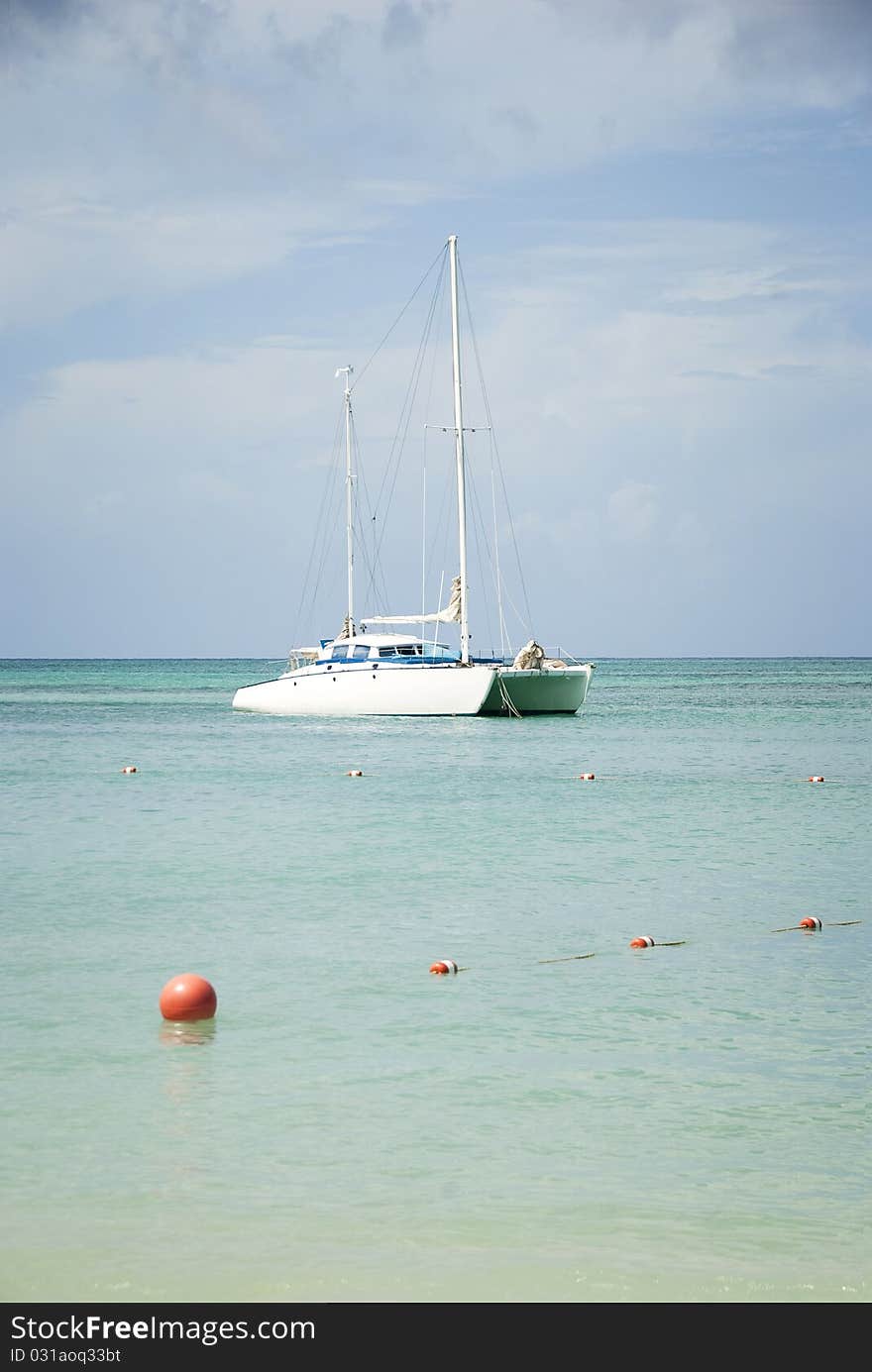 A white catamaran sailboat anchored off shore in the Caribbean.