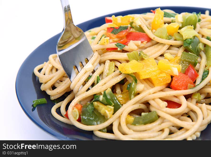 Spaghetti with vegetables being eaten with a fork on white background