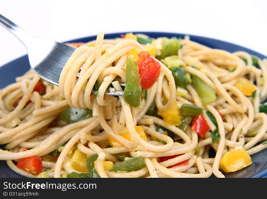 Spaghetti with vegetables being eaten with a fork on white background