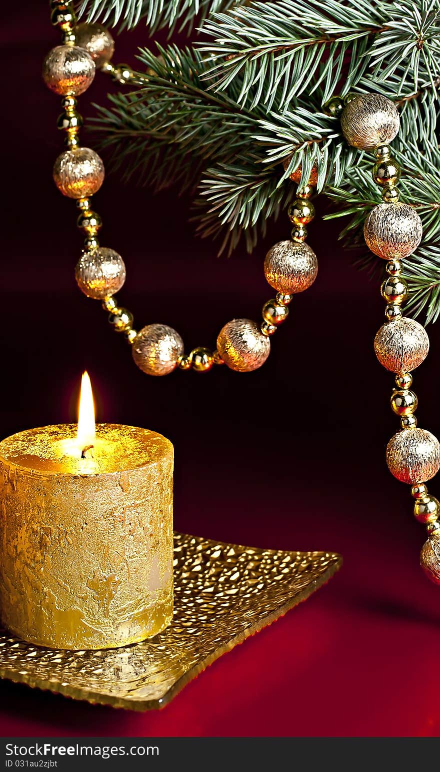 On a red background, a burning candle, fir branch and a ball chain. On a red background, a burning candle, fir branch and a ball chain.