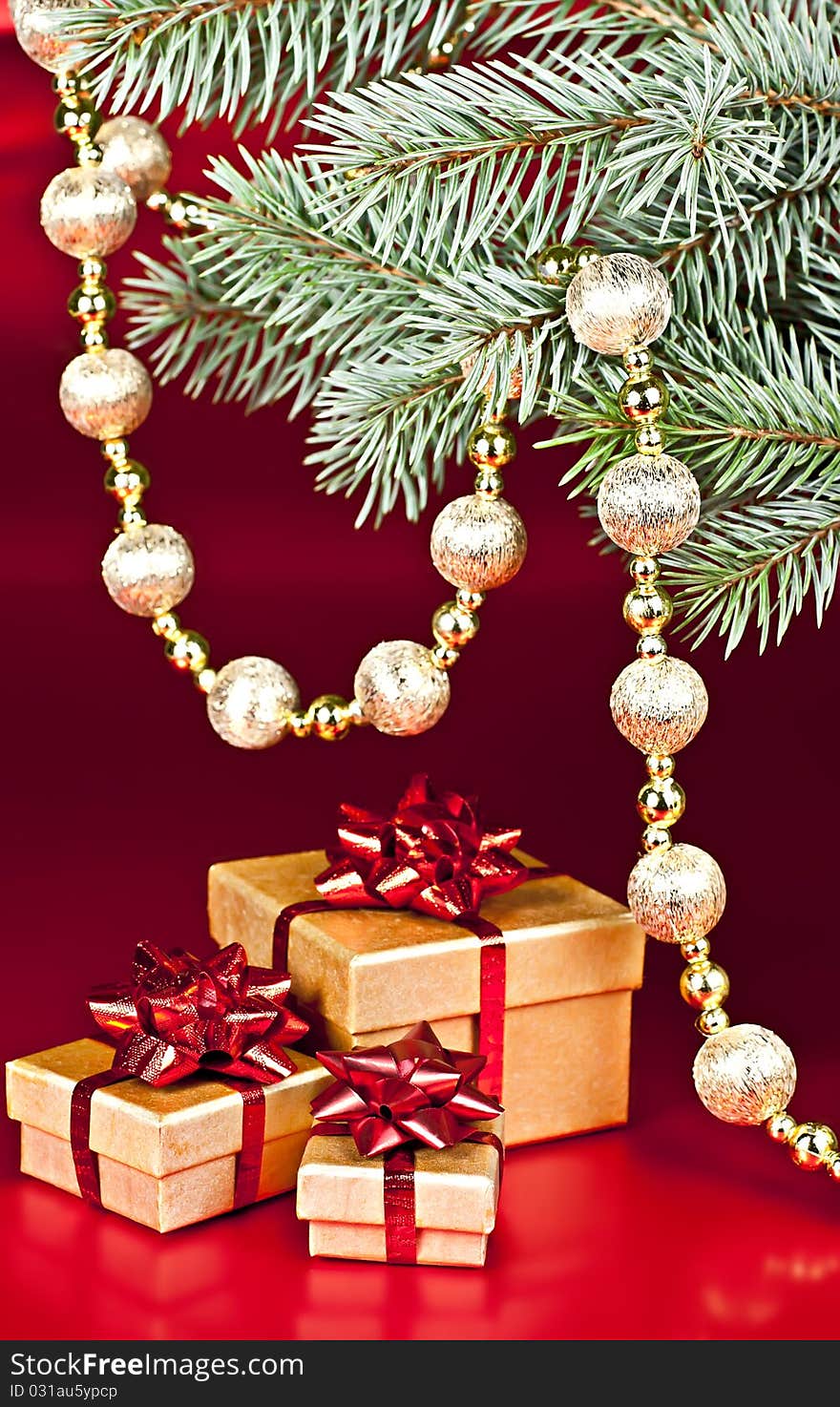 On a red background with a spruce twig Christmas decoration ball on a string of gift boxes. On a red background with a spruce twig Christmas decoration ball on a string of gift boxes.