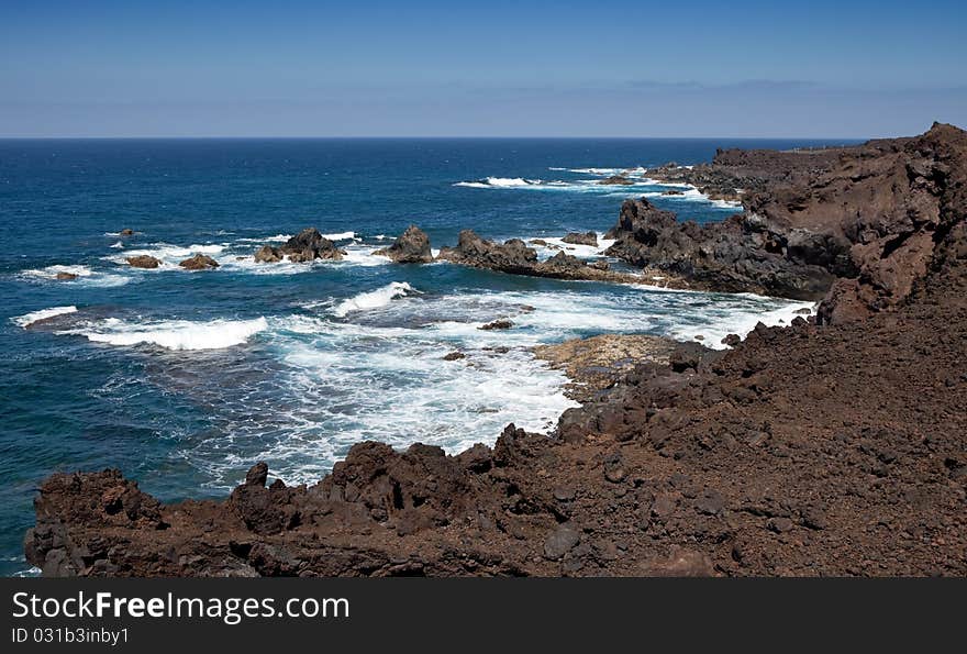 Lanzarote coastline, black rocks on blue sea and sky background, Spain