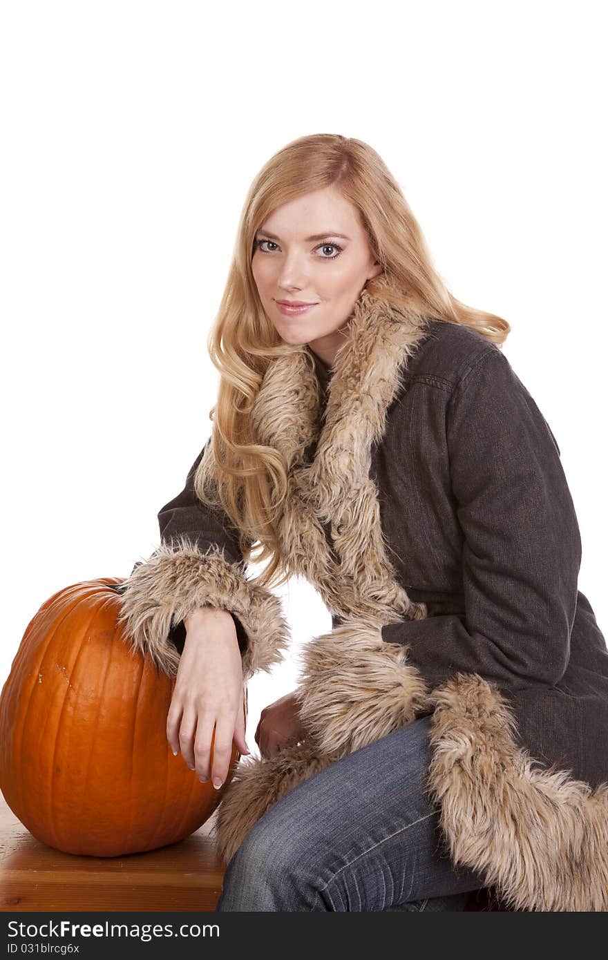 A woman sitting in her warm fuzzy coat while she leans on a pumpkin. A woman sitting in her warm fuzzy coat while she leans on a pumpkin.