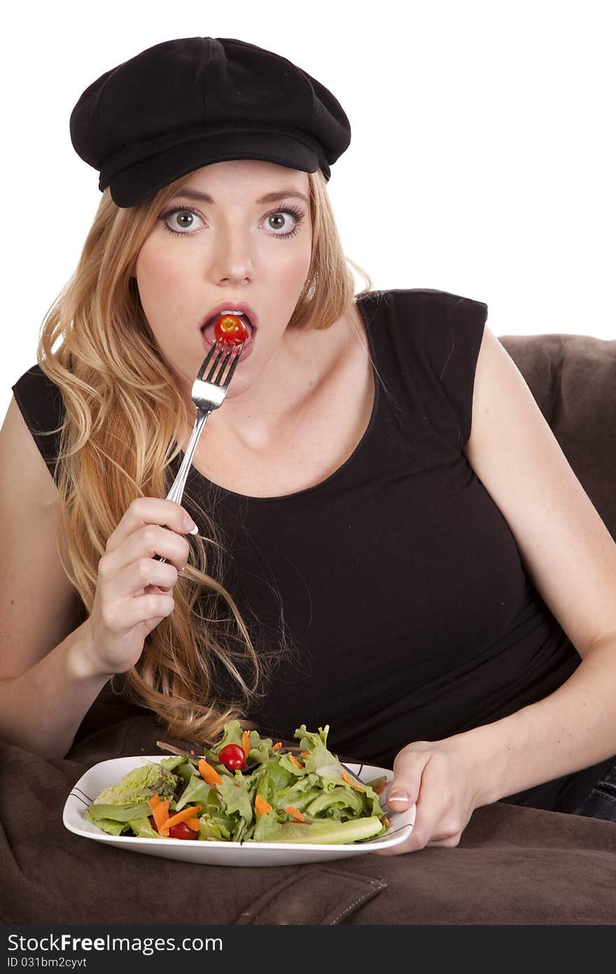 A woman sitting on a bean bag getting ready to eat a tomato while she is enjoying her nice green salad. A woman sitting on a bean bag getting ready to eat a tomato while she is enjoying her nice green salad.