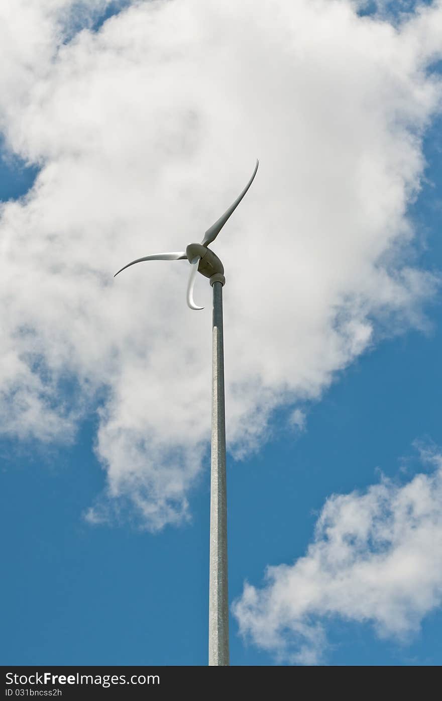 A spinning windmill with curved blades turns in front of a blue sky and white clouds. A spinning windmill with curved blades turns in front of a blue sky and white clouds.