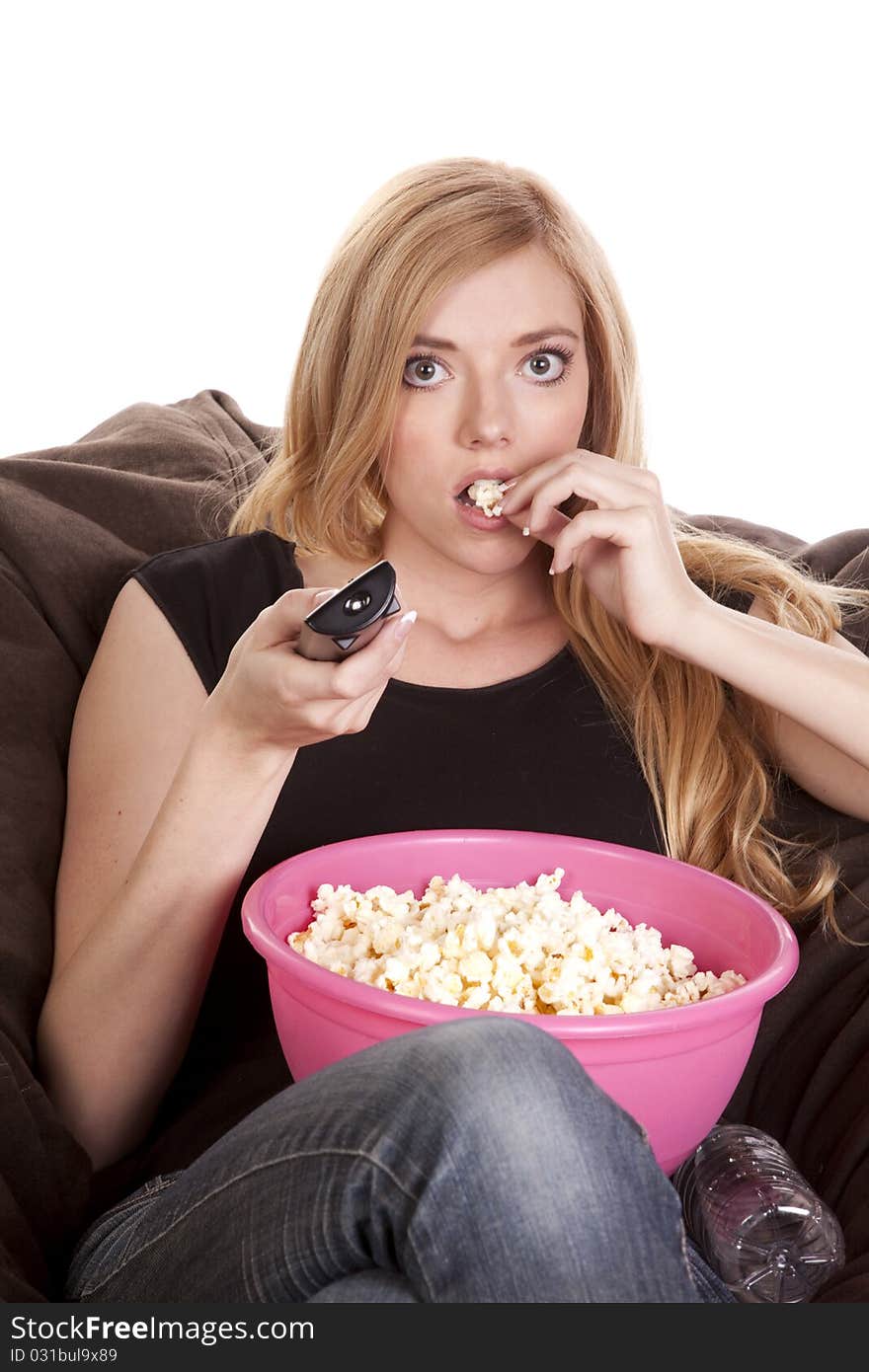 A woman sitting on a bean bag while she is enjoying her popcorn while she is watching tv with intense eyes. A woman sitting on a bean bag while she is enjoying her popcorn while she is watching tv with intense eyes.