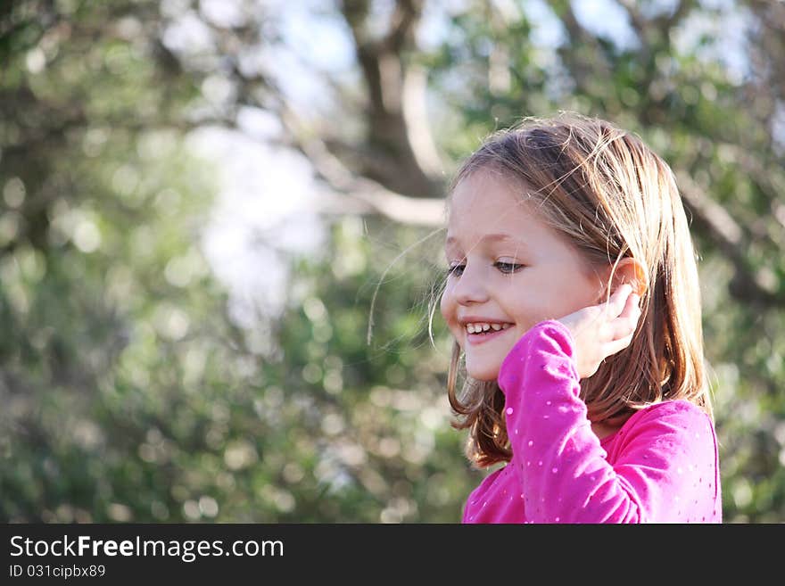 Profile portrait of a happy female child smiling outdoors with natural bokeh background