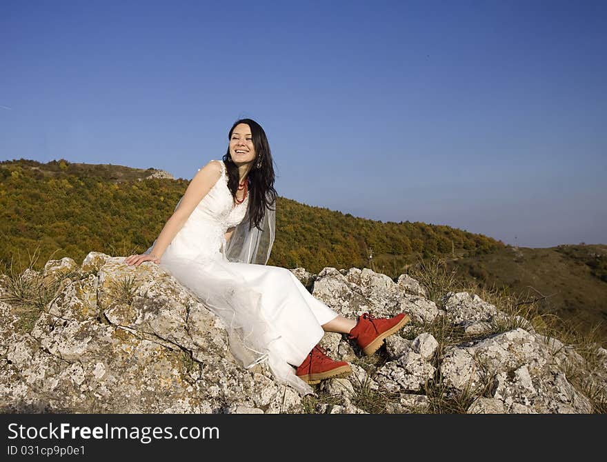 Romantic woman with red boots sitting on rocks