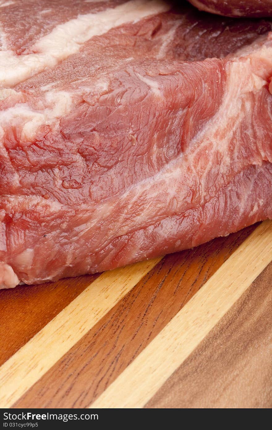 A piece of raw meat on a multilayer wooden kitchen cutting board.