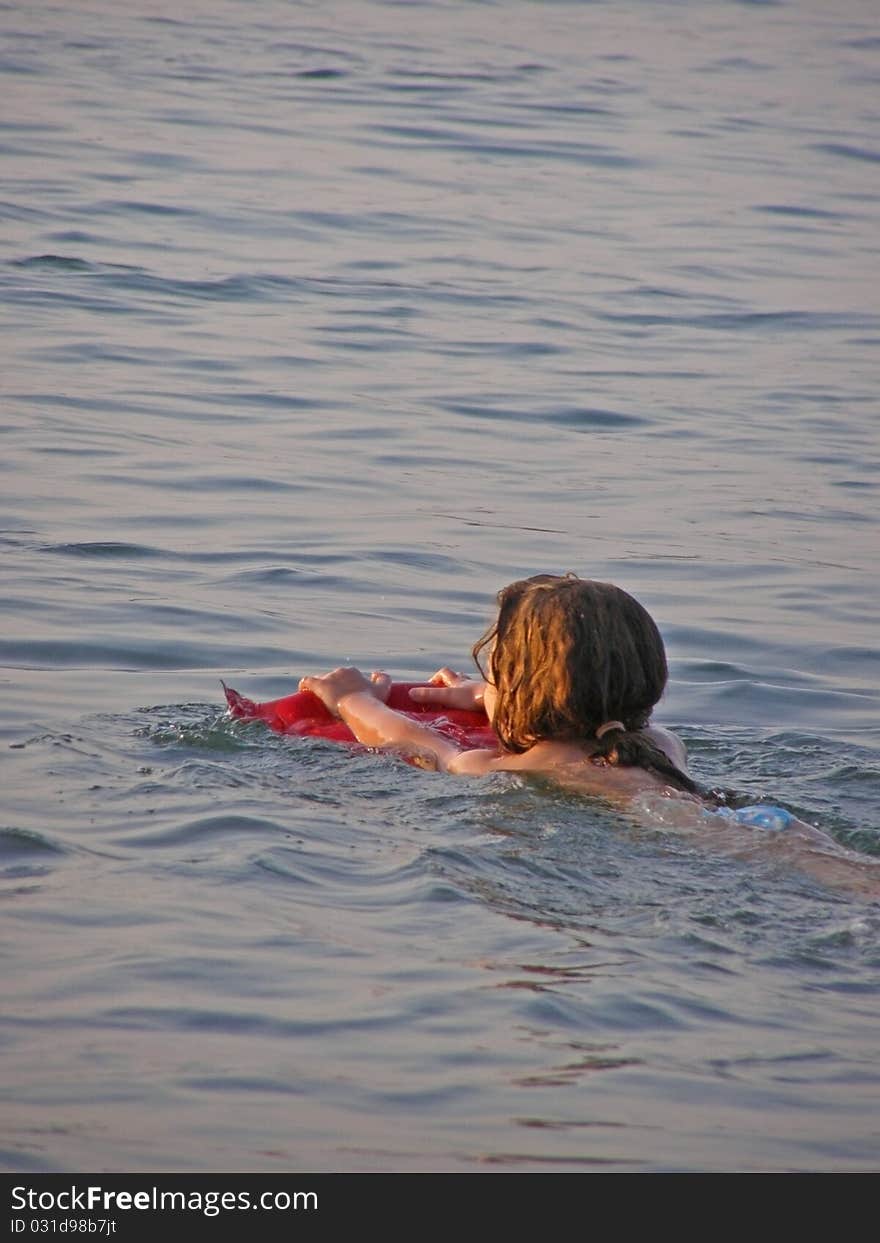 Preschooler child learning to swim, swimming away with the aid of the floating pillow in the sea at sunset; *with space for text (copyspace)