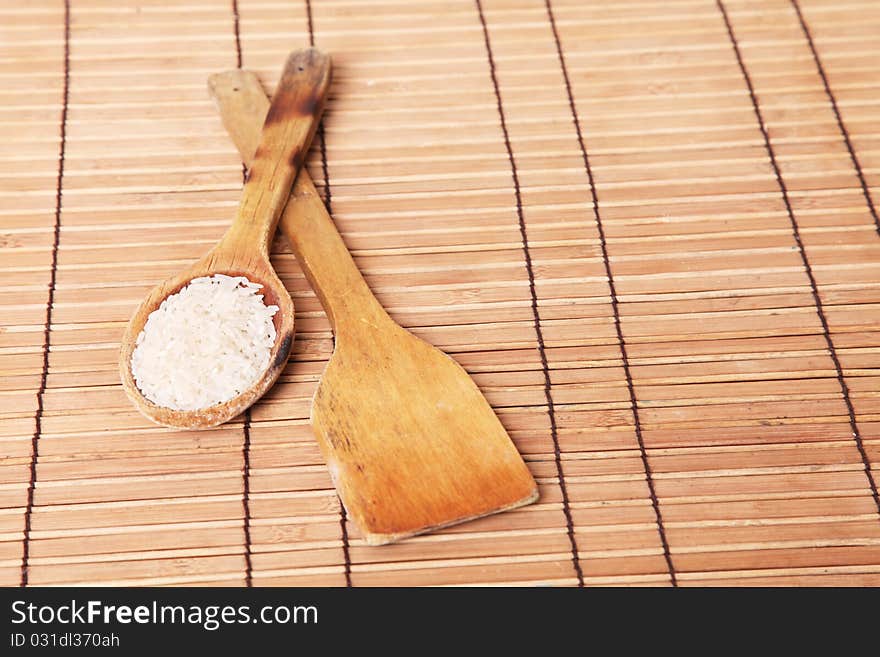 Wooden spoon with rice and wooden scoop empty over bamboo sticks background