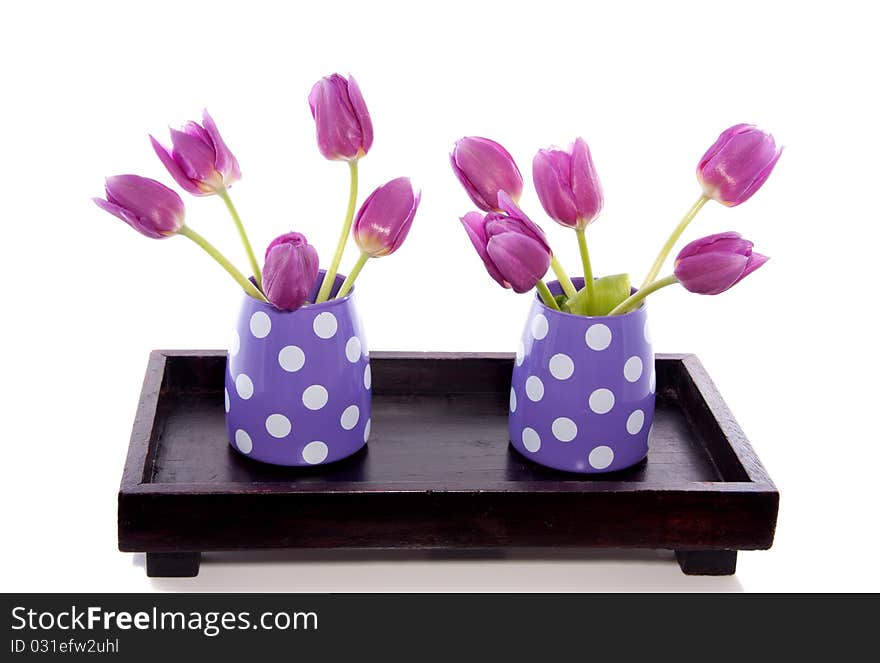 Two little vases with purple tulips on a wooden tray isolated over white