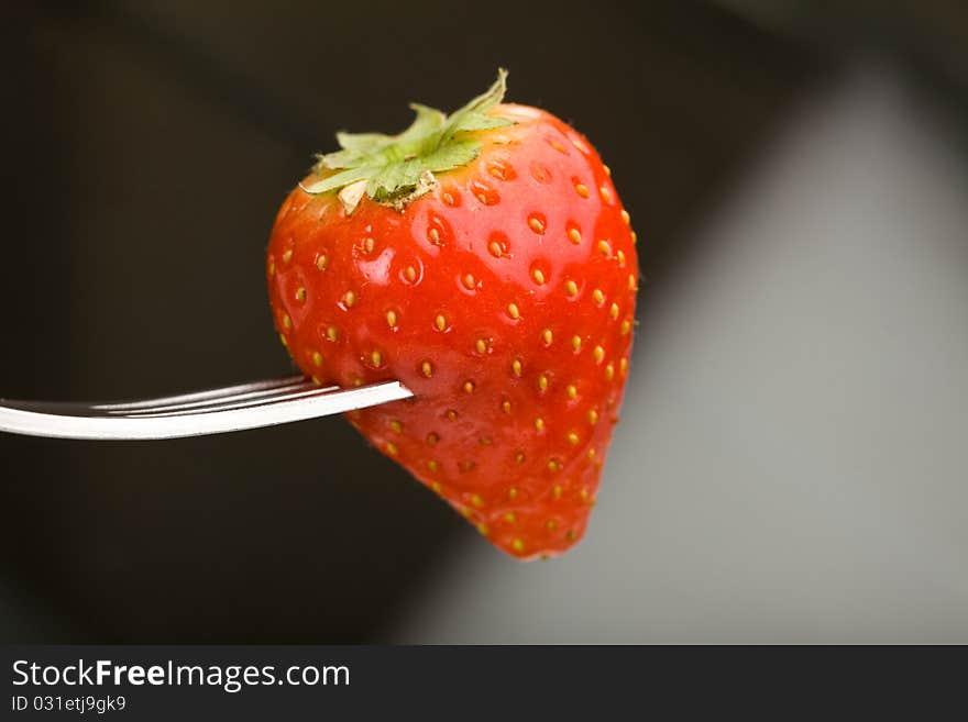 Photo of strawberry holded by a fork in front of an dark abstract background