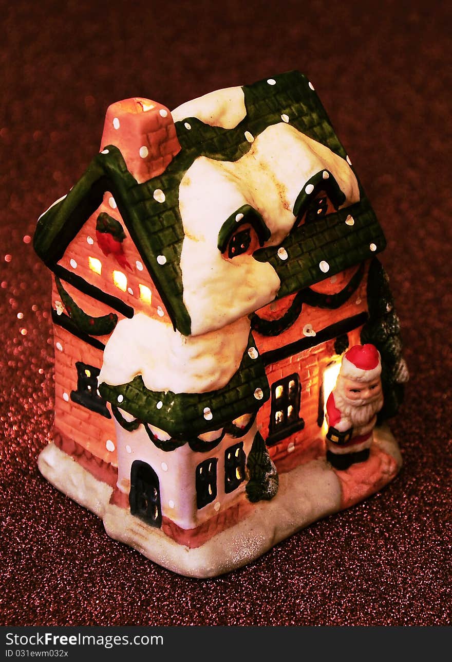 Chtistmas little toy house with Santa Claus and candle inside the house on the brown shiny twinkly background