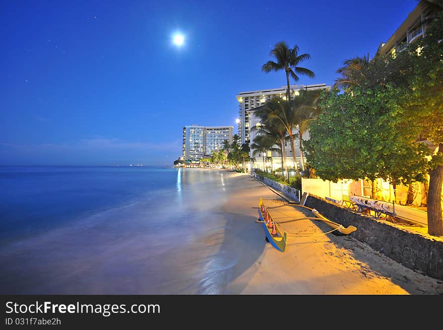 An outrigger in the sandy beach with full moon and hotels. An outrigger in the sandy beach with full moon and hotels