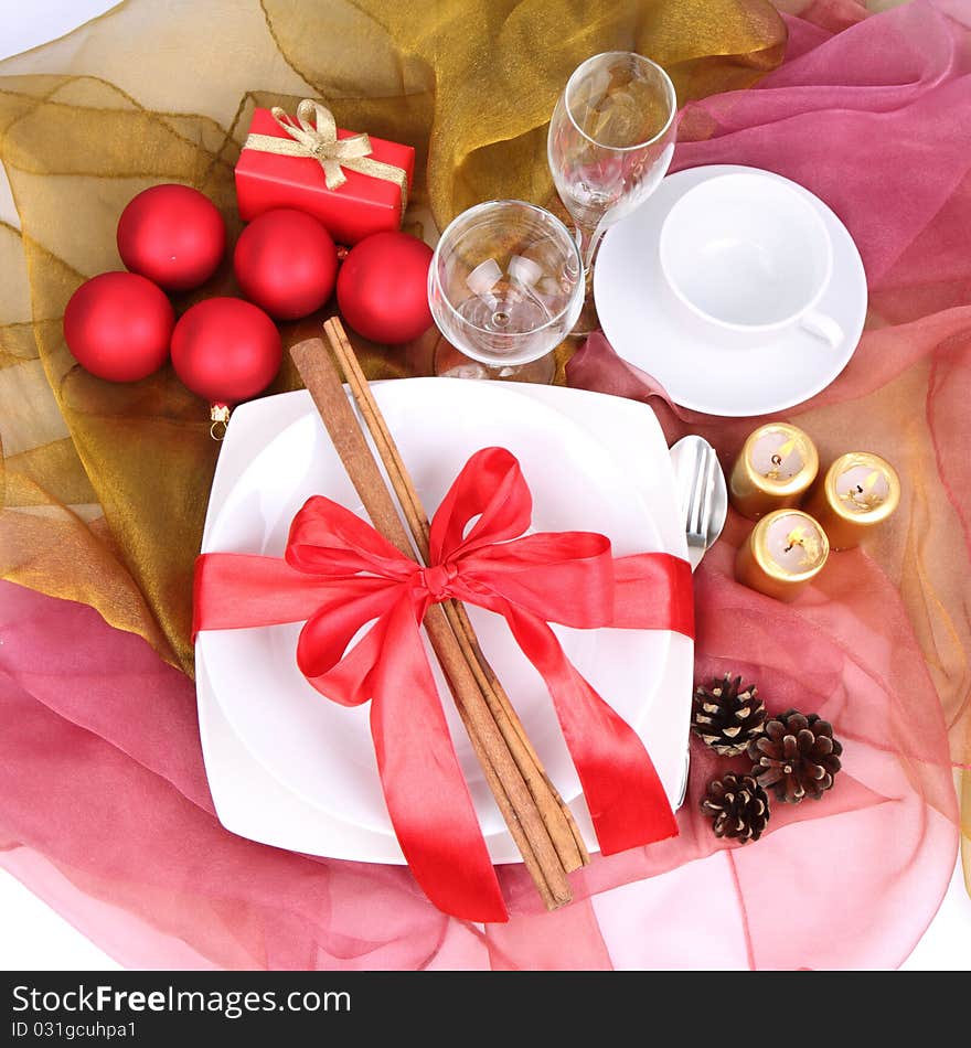 Christmas setting-a plate decorated with cinnamon sticks and ribbon, a cup, glasses, christmas balls, candles, gift and cones