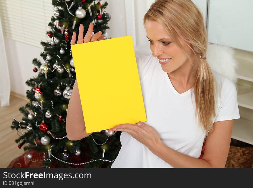 blond angel standing in front of a christmas tree holding a sign. blond angel standing in front of a christmas tree holding a sign