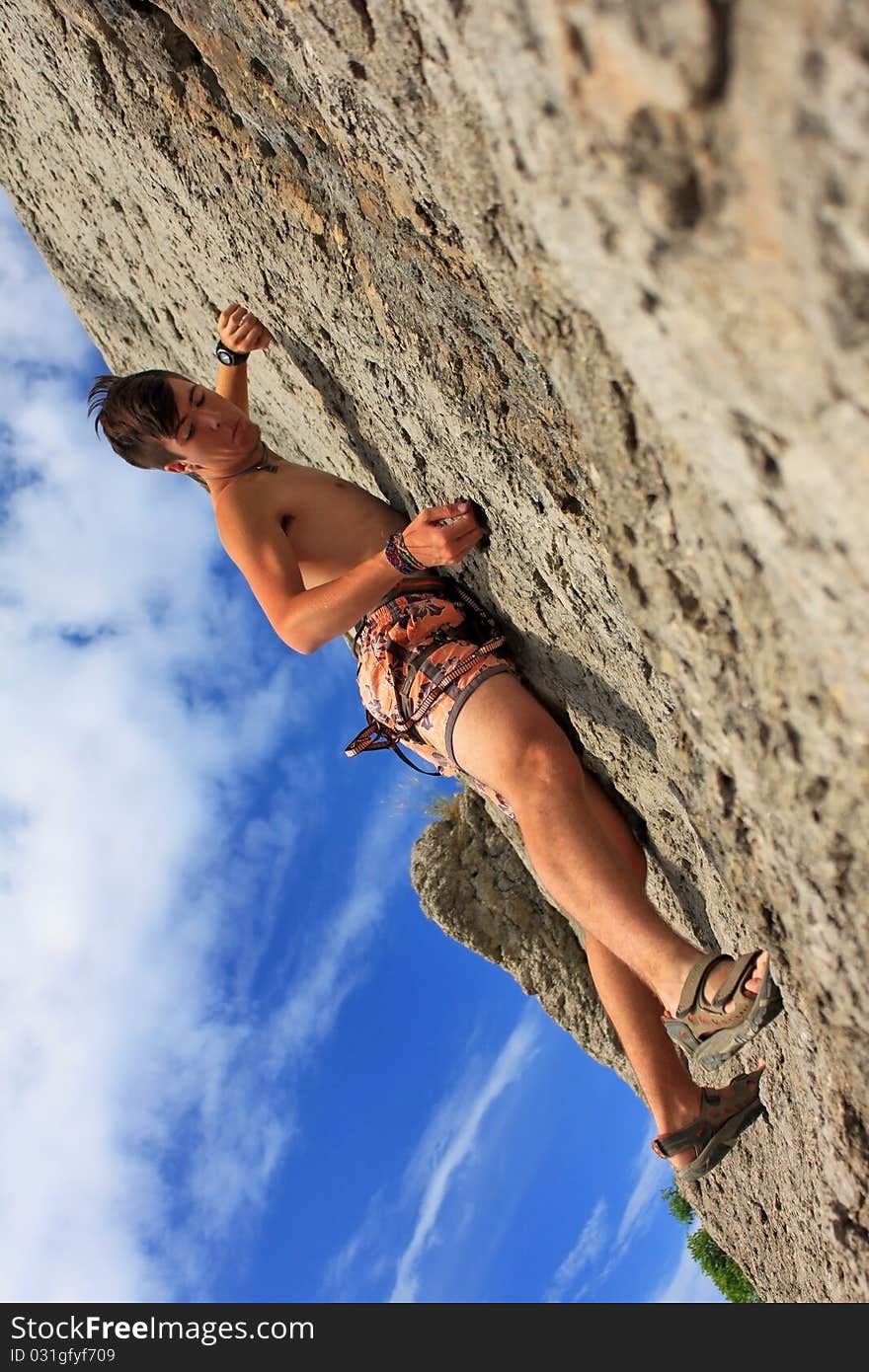 A guy climbs on a rock against the blue sky. A guy climbs on a rock against the blue sky