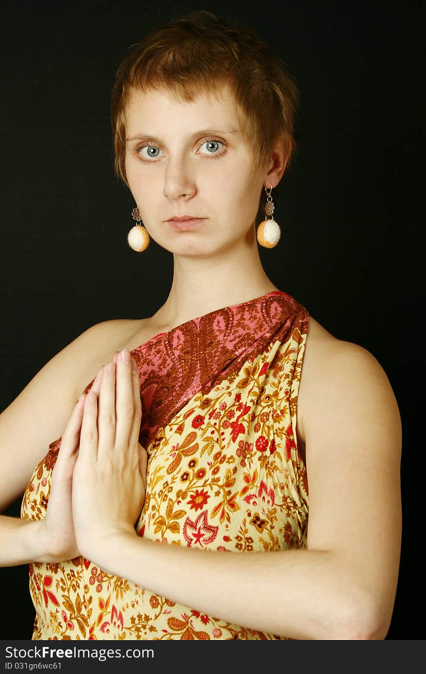 Young woman with bare shoulders in her wearing earrings made of wool. Hands folded in prayer. Buddhism