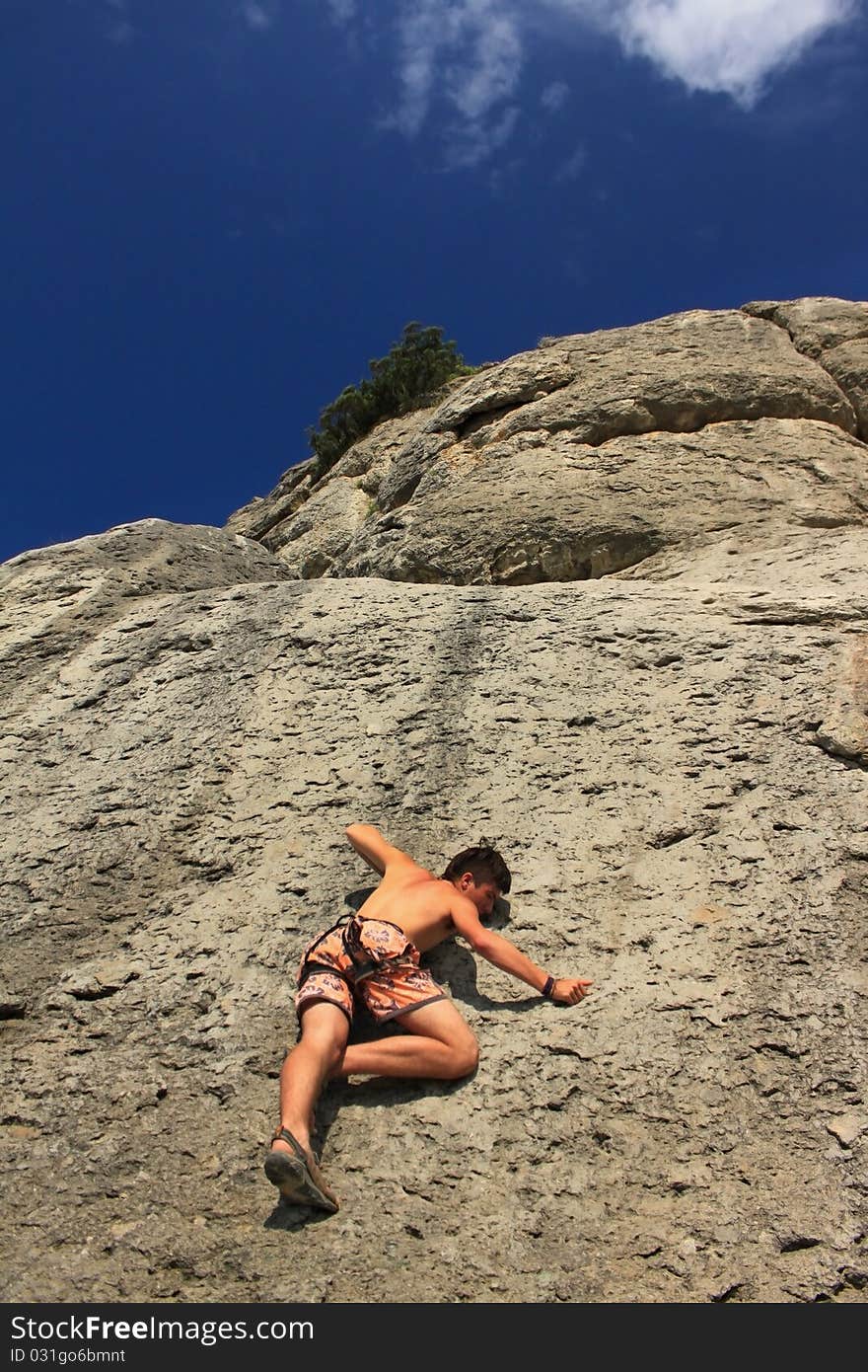 A guy climbs on a rock against the blue sky. A guy climbs on a rock against the blue sky